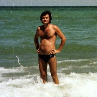 Man stands in shallow water on a sunny beach.