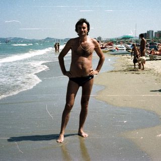 Man stands on a crowded beach with the ocean behind.
