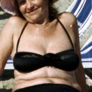 Woman sits on a beach with lounge chairs and hotel.