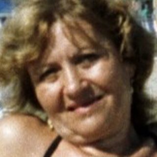 Woman sits on a beach with lounge chairs and hotel backdrop.