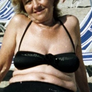 Woman sits on a beach with lounge chairs and hotel backdrop.