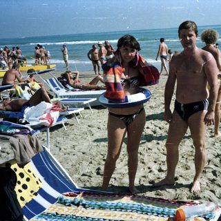 People on a crowded beach with sun loungers and waves.