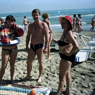 People on a crowded beach with sun loungers and waves.
