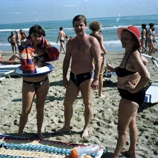 People on a crowded beach with sun loungers and waves.