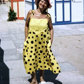Woman stands near colorful beach huts on a sunny day.