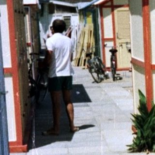Woman stands near colorful beach huts on a sunny day.