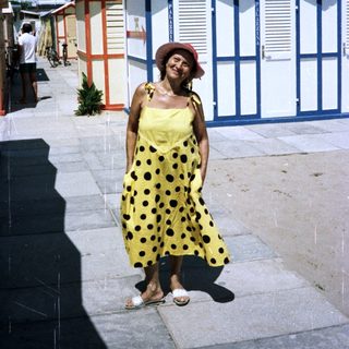 Woman stands near colorful beach huts on a sunny day.