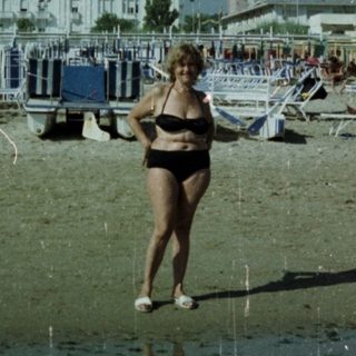Woman stands on beach with hotel and people in background.