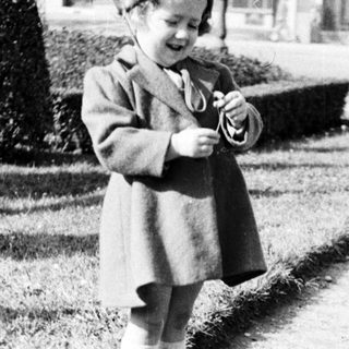 Here's a brief summary of the image: Young child in coat stands near a garden path.