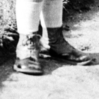 Here's a brief summary of the image: Young child in coat stands near a garden path.