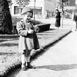 Here's a brief summary of the image: Young child in coat stands near a garden path.