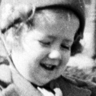Here's a brief summary of the image: Young child in coat stands near a garden path.