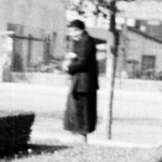 Here's a brief summary of the image: Young child in coat stands near a garden path.