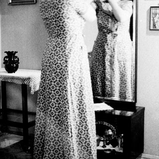 Woman in dress adjusting it in front of a mirror.