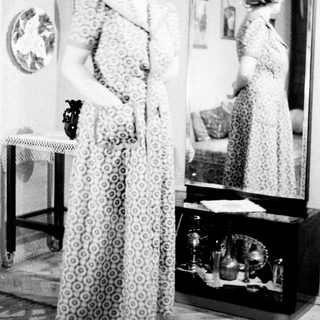 Woman stands before a mirror in a patterned dress.