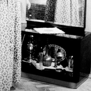 Woman stands before a mirror in a patterned dress.