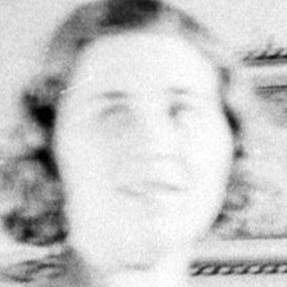 Woman stands before a mirror in a patterned dress.