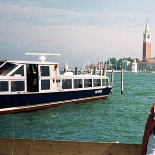 Here's a brief summary of the image: Three people pose near water with Venice in the background.