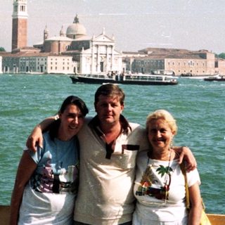 Here's a brief summary of the image: Three people pose near water with Venice in the background.