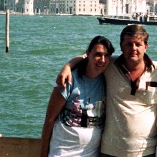 Here's a brief summary of the image: Three people pose near water with Venice in the background.