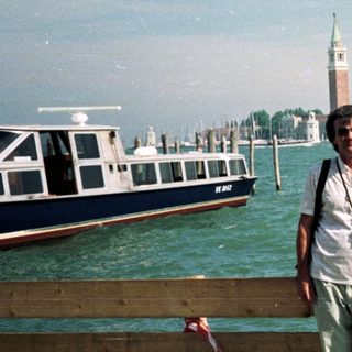 Couple poses near water with San Giorgio Maggiore in background.