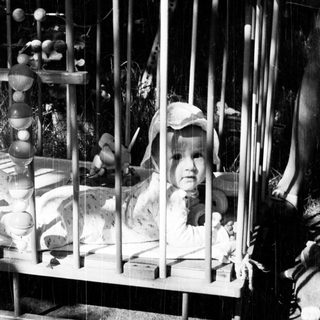 Baby in a crib with wooden toys and a hat.