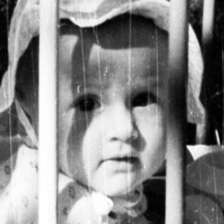 Baby in a crib with wooden toys and a hat.