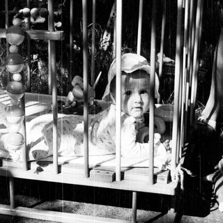 Baby in a crib with wooden toys and a hat.