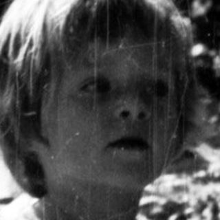 Here's a brief summary of the image: Child stands in rain, appearing surprised in a garden.