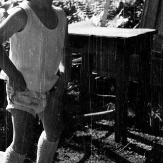 Here's a brief summary of the image: Child stands in rain, appearing surprised in a garden.