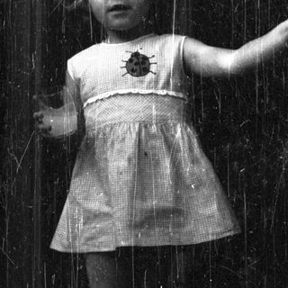 Here's a brief summary of the image: Girl stands near a door, peering out with a concerned expression.