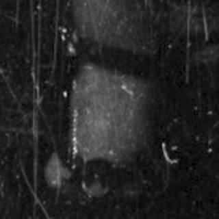Here's a brief summary of the image: Girl stands near a door, peering out with a concerned expression.