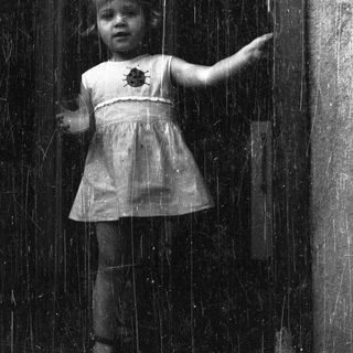 Here's a brief summary of the image: Girl stands near a door, peering out with a concerned expression.