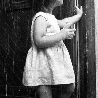 Here's a brief summary of the image: A young child stands reaching for a door handle.