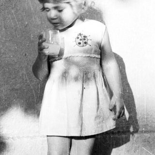 Here's a brief summary of the image: Young child stands holding a glass, casting a shadow.