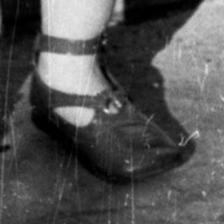 Here's a brief summary of the image: Young child stands holding a glass, casting a shadow.