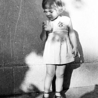 Here's a brief summary of the image: Young child stands holding a glass, casting a shadow.