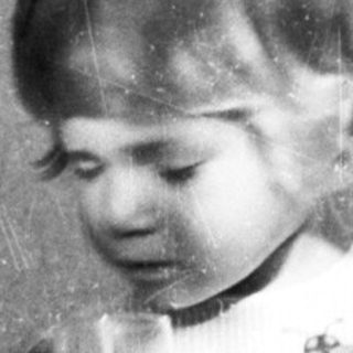 Here's a brief summary of the image: Young child stands holding a glass, casting a shadow.