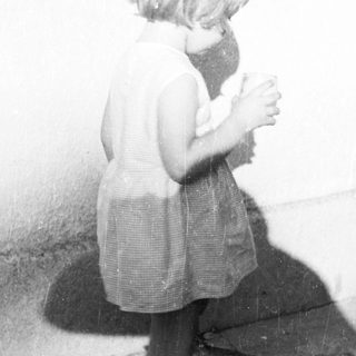 Here's a brief summary of the image: Young child stands with a cup, casting a shadow.