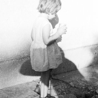 Here's a brief summary of the image: Young child stands with a cup, casting a shadow.