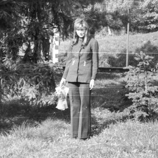 Woman and man stand in a grassy, wooded area.