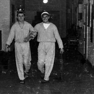 Two men in uniforms walk down a hallway.