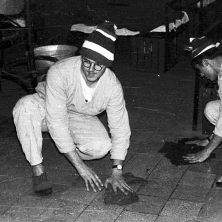 Two men in uniform crouch, examining something on the ground.