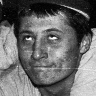 Two men in hats sit close together, looking at the camera.