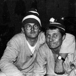 Two men in hats sit close together, looking at the camera.