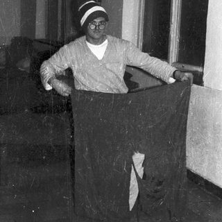 Man standing with fabric, wearing glasses and hat.