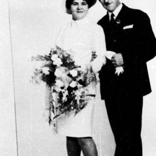 Couple in formalwear poses with flowers, likely a wedding.