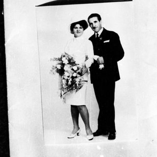 Couple in formalwear poses with flowers, likely a wedding.