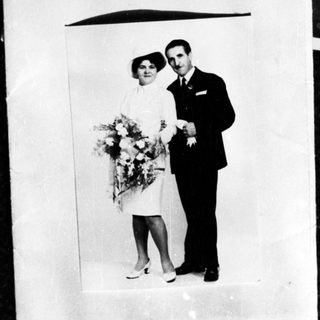 Couple in formalwear poses with flowers, likely a wedding.