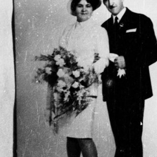 Couple in formal wear poses with flowers, likely a wedding.